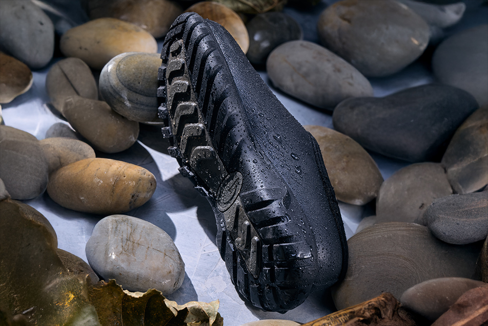 Grubs Waterline waterproof shoe showing rugged tread and water droplets among wet rocks.