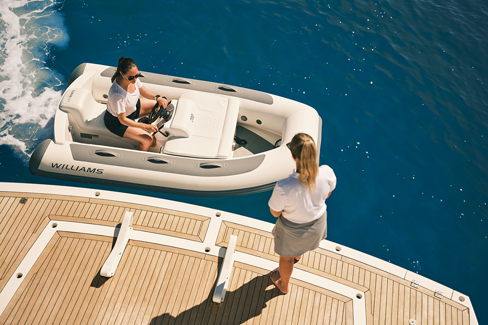 Aerial view of a Williams jet tender moored alongside a yacht, driver aboard, woman on teak deck.