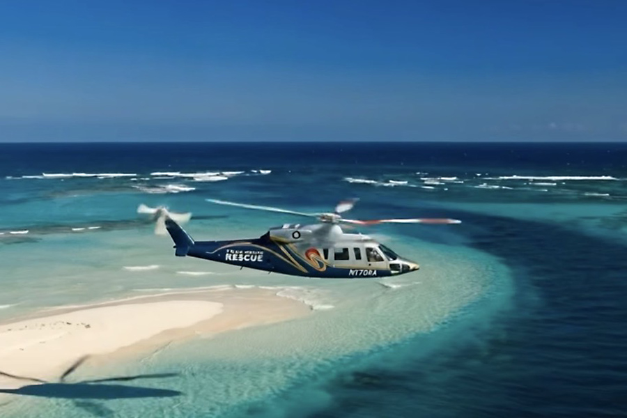 Tropic Air Rescue helicopter flying over turquoise Bahamas waters during an air ambulance mission.
