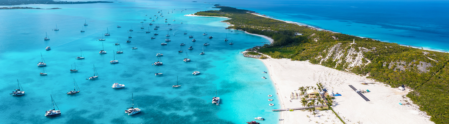 Boats anchored off a white-sand Bahamas island, highlighting the remoteness of cruising in turquoise waters.