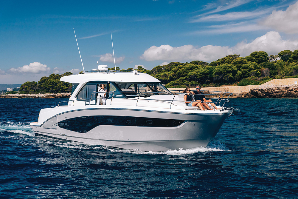 Beneteau Antares 12 motor cruiser making way with a sand beach and trees behind