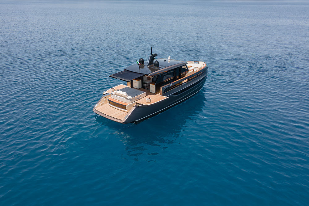 Overhead shot of a dark-hulled motor yacht with teak deck trim and roof-mounted solar panels on open blue water.