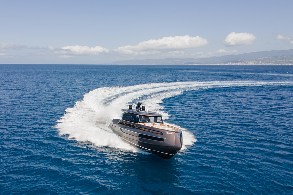 Bronze-hulled motor yacht at speed, carving a sharp turn with a wide wake off a mountainous coastline.