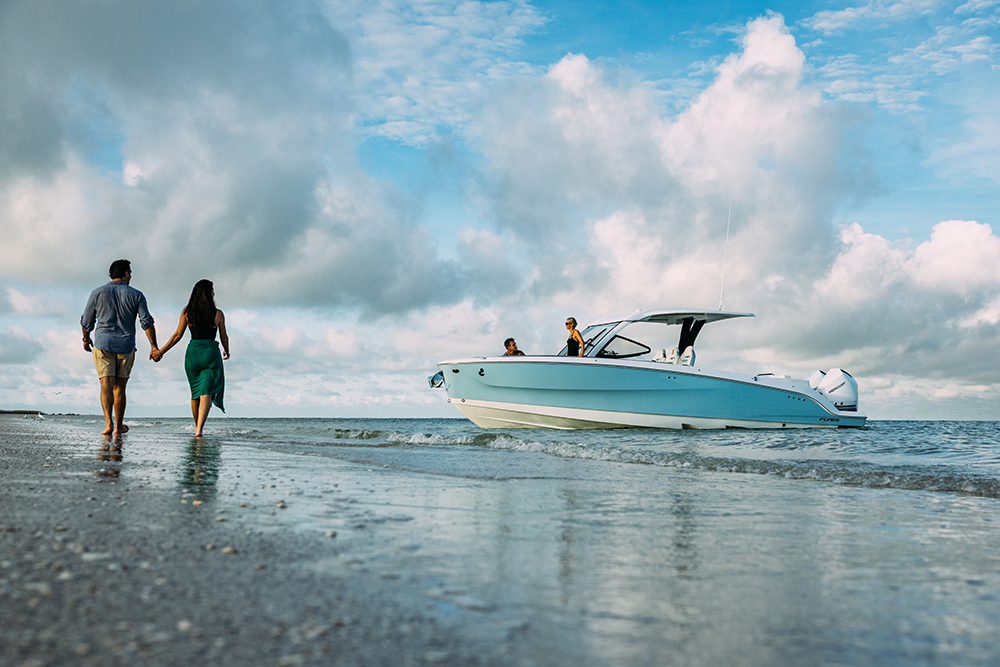 Couple walking hand in hand on the beach as a white and pale-blue outboard day boat idles near the shoreline.