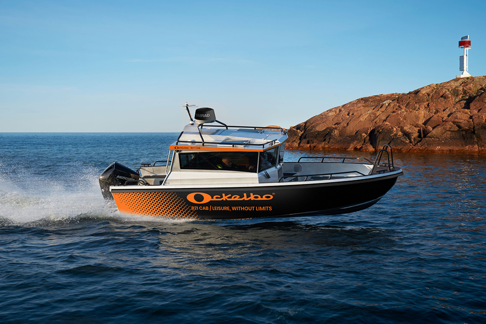 Ockelbo B21 cabin powerboat with Mercury outboard running past a rocky shoreline and navigation marker