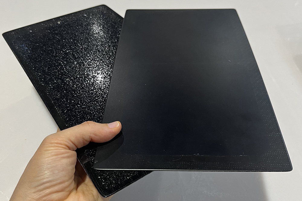 Hand holding two Praxis solar panel samples, comparing a textured matte finish with a glossy surface.