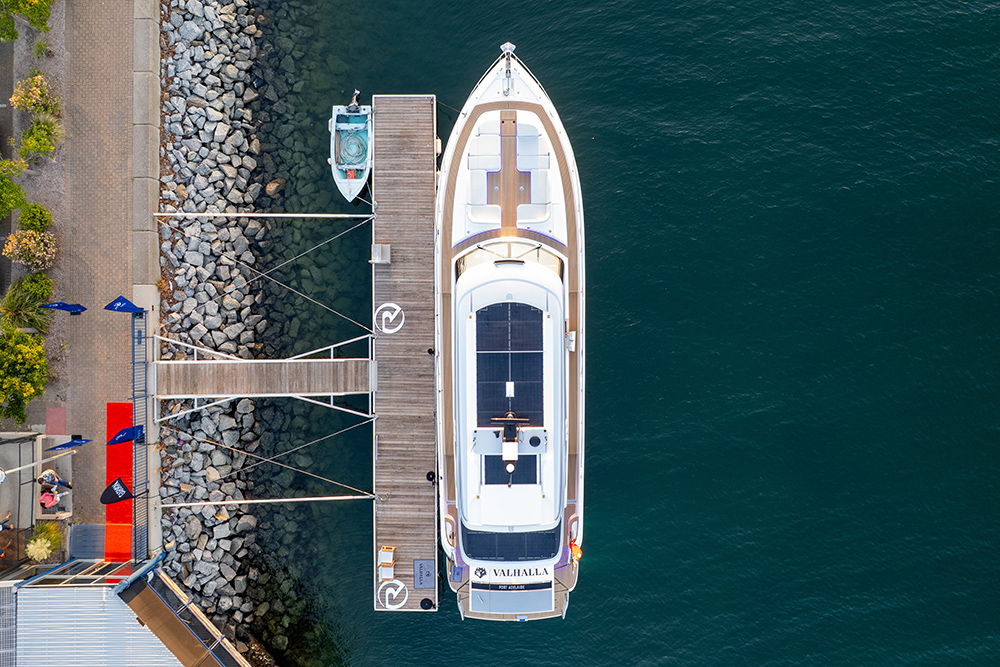 Aerial view of Riviera 6800 motor yacht Valhalla moored at a marina berth, solar panel visible on the foredeck.