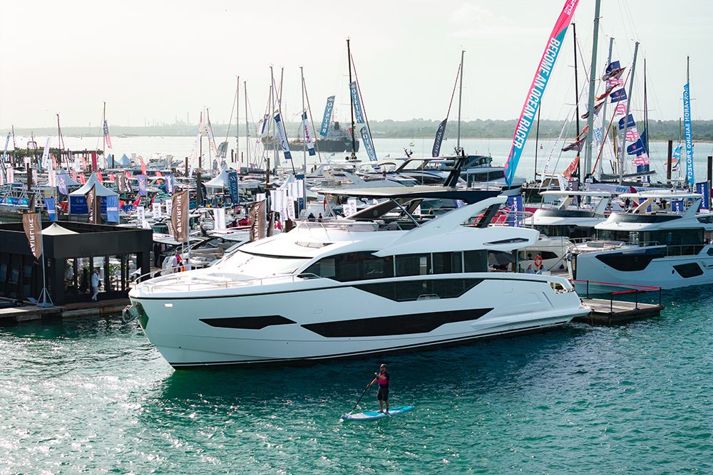 Paddleboarder beside a large white motor yacht in the crowded show marina at Southampton International Boat Show