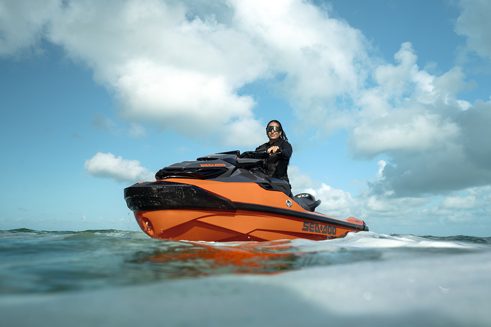 Rider on a black and orange Sea-Doo personal watercraft crossing open water under a blue sky