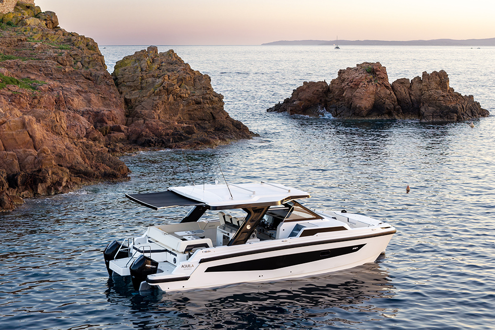 Aquila 35 Sport power catamaran with hardtop and twin Mercury outboards on calm water beside red rocks at golden hour