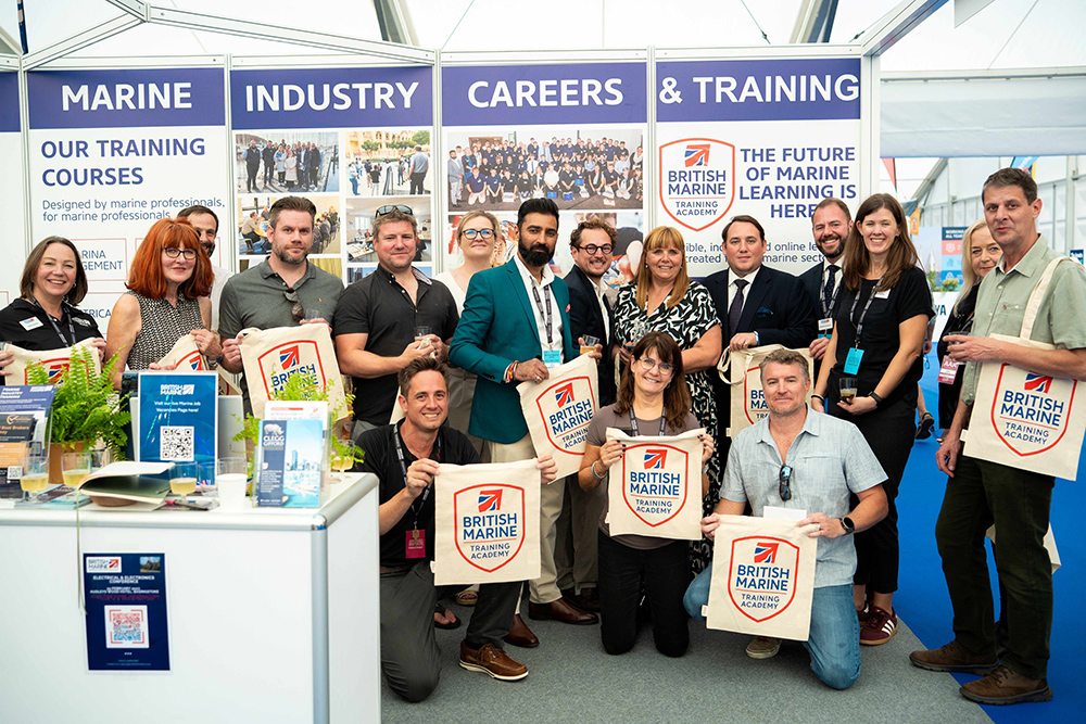 Group holding British Marine Training Academy tote bags on the marine careers and training stand at Southampton Boat Show