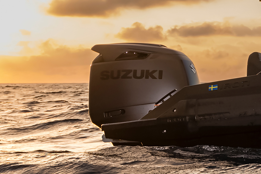 Suzuki outboard engine on the stern of a dark grey RIB at sea, against a golden sunset sky