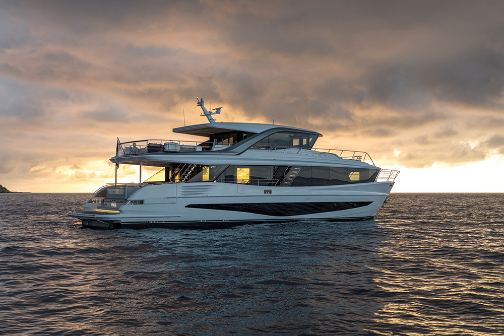 Princess Yachts X90 a white flybridge motor yacht on calm open water at sunset, its lit saloon glowing beneath dramatic golden clouds.