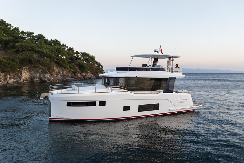 White Sirena 48 motor yacht on calm water beside a wooded headland at dusk, with two people on its flybridge.