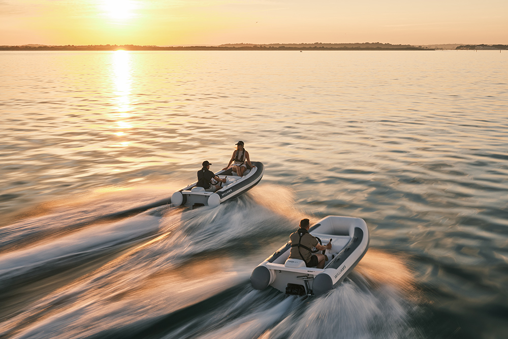 Two Williams TurboJet MX jet tenders speed across calm water at sunset, leaving wakes glowing in golden light